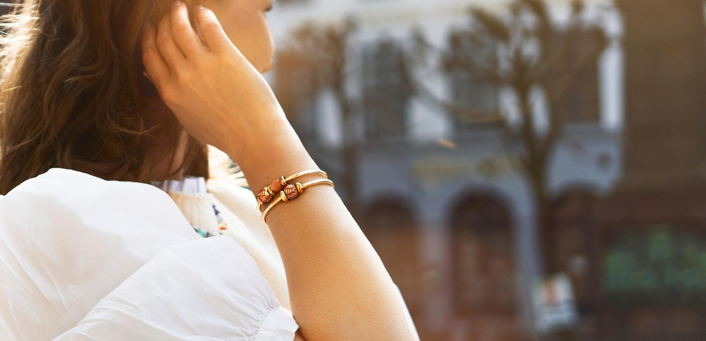 Close up of two gold plated bangles styled with beads in summer sunlight